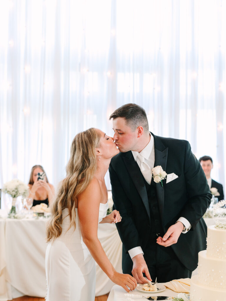 Couple sharing a kiss during cake cutting at Arrowhead Golf Club wedding reception, romantic moment captured beautifully.